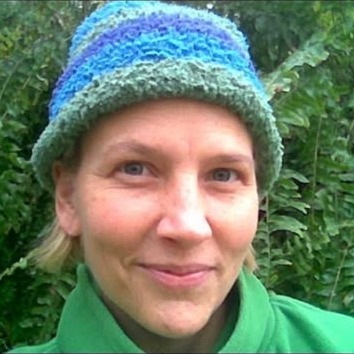 Heather smiling outdoors in a blue knitted hat and green jacket